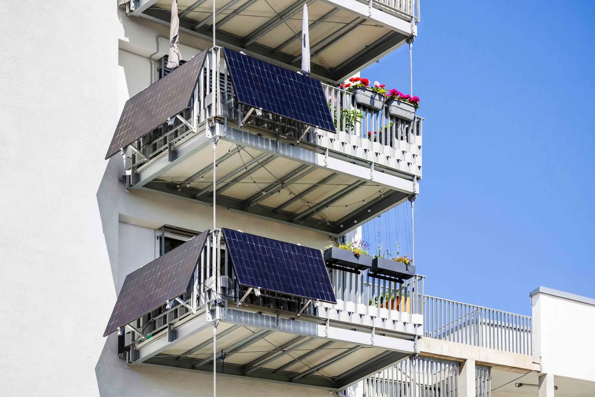 Balkone eines weißen Gebäudes mit Solarpaneelen und Blumenkästen unter einem klaren blauen Himmel.