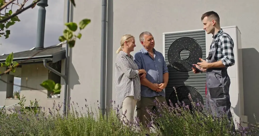Ein Techniker bespricht eine Außeneinheit einer Wärmepumpe mit einem Paar.