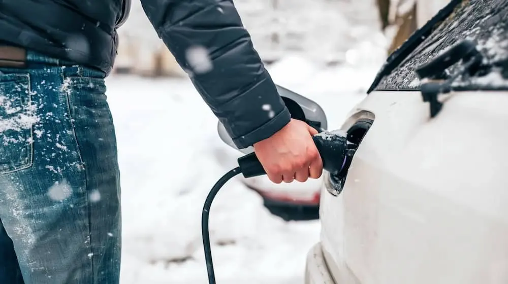 Eine Person steckt ein Elektroauto im Schnee an eine Ladestation.