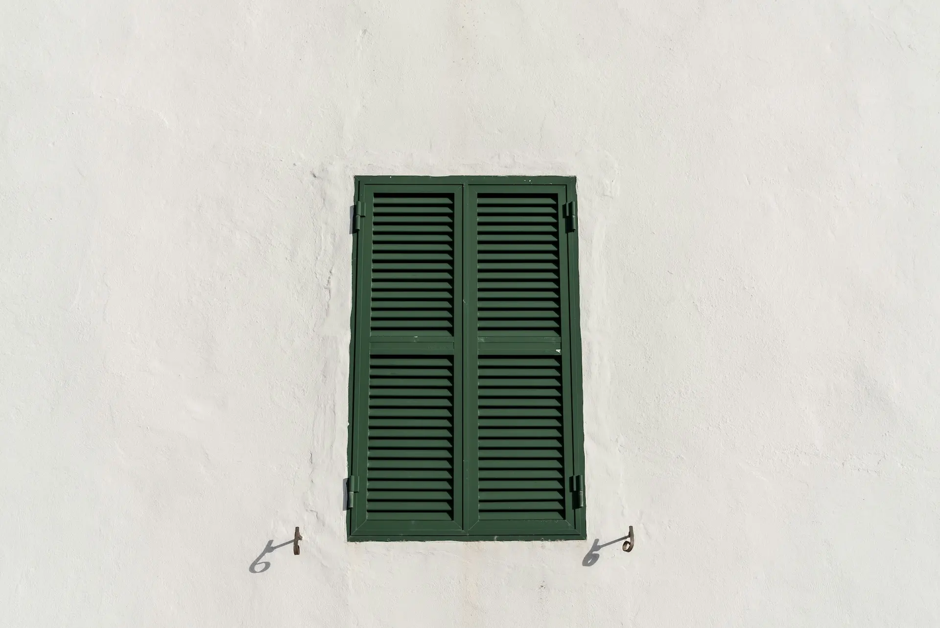 Das Bild zeigt einen geschlossenen, grünen Fensterladen an einer weißen Fassade, vermutlich in einem südeuropäischen Land.