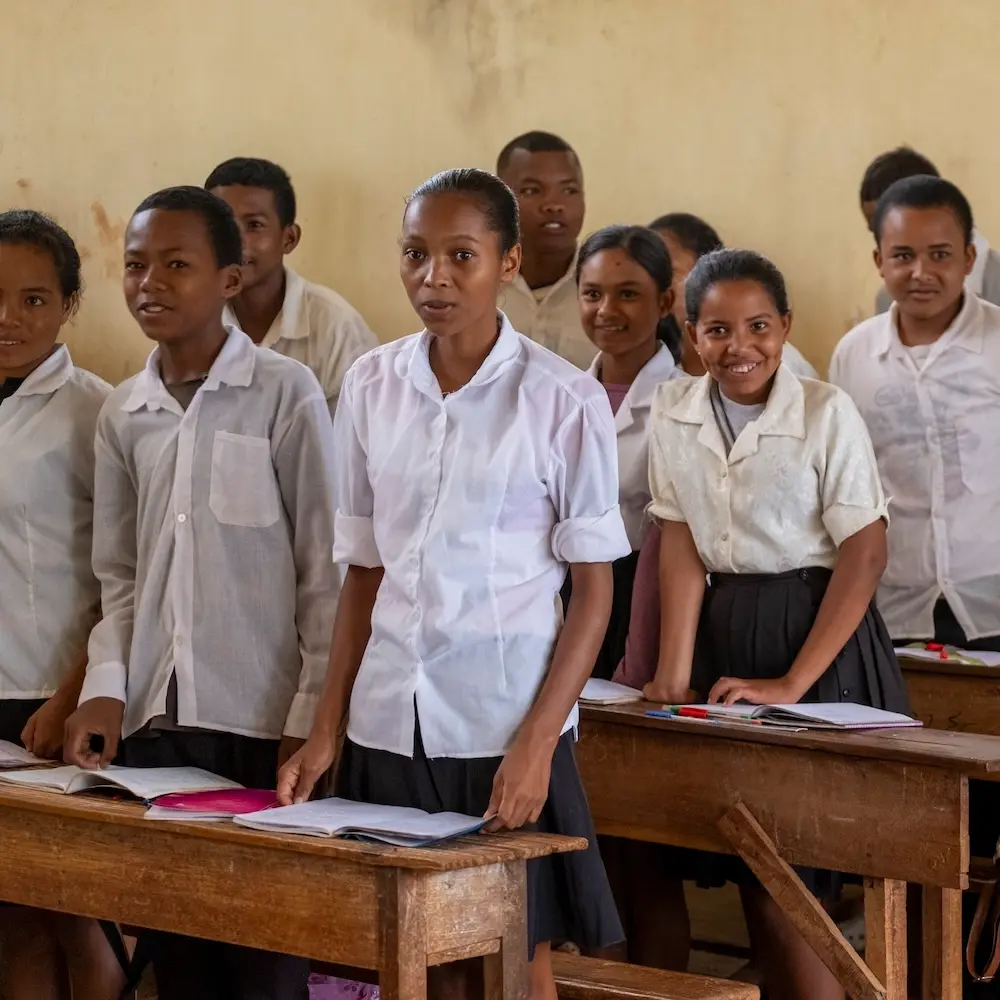 Schüler:innen in einer Schulkasse in Madagaskar stehen hinter ihren Pulten