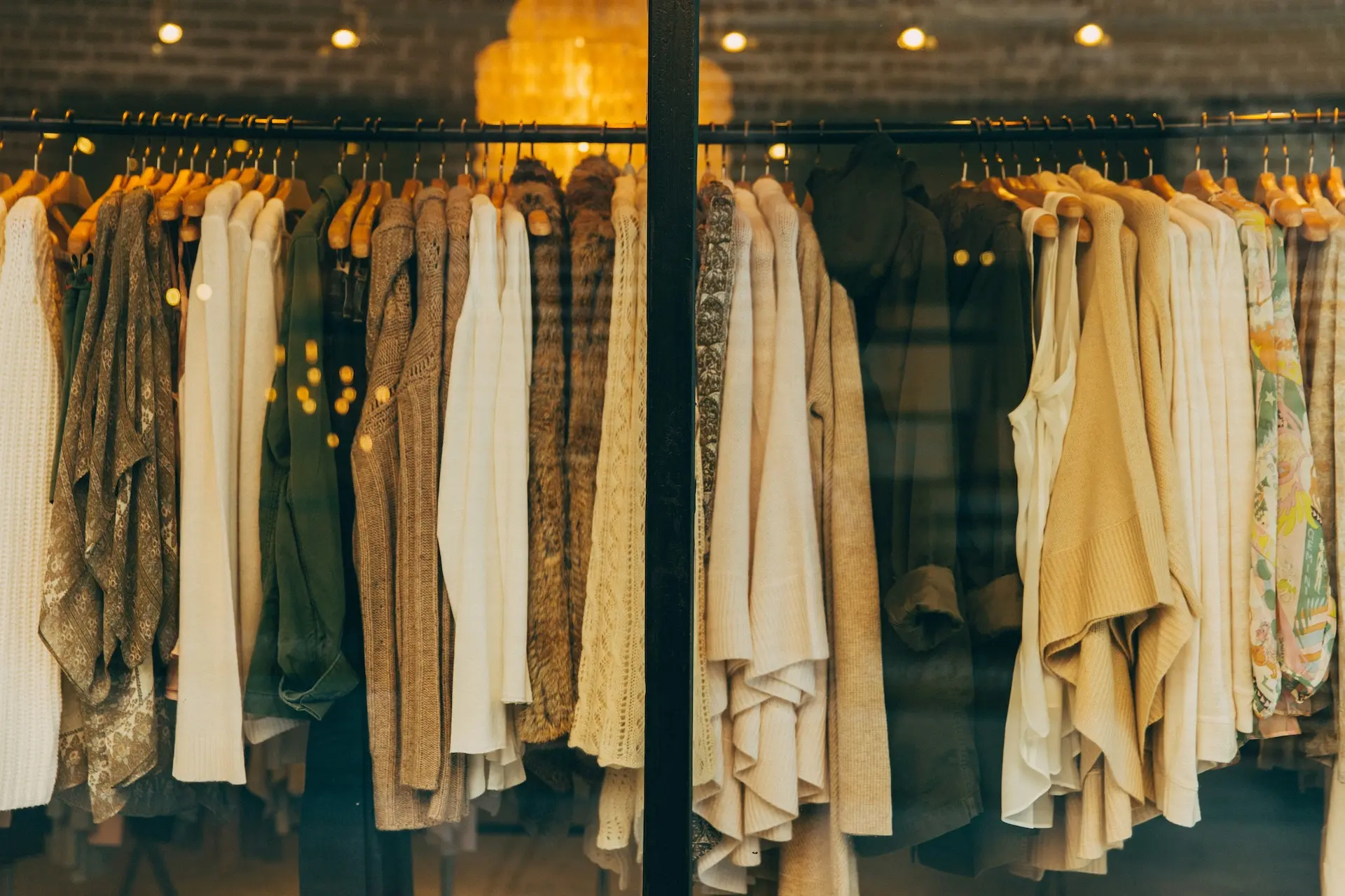 Ein Kleiderständer mit Pullovern und Strickjacken in neutralen Farben, die in einem Schaufenster ausgestellt sind.