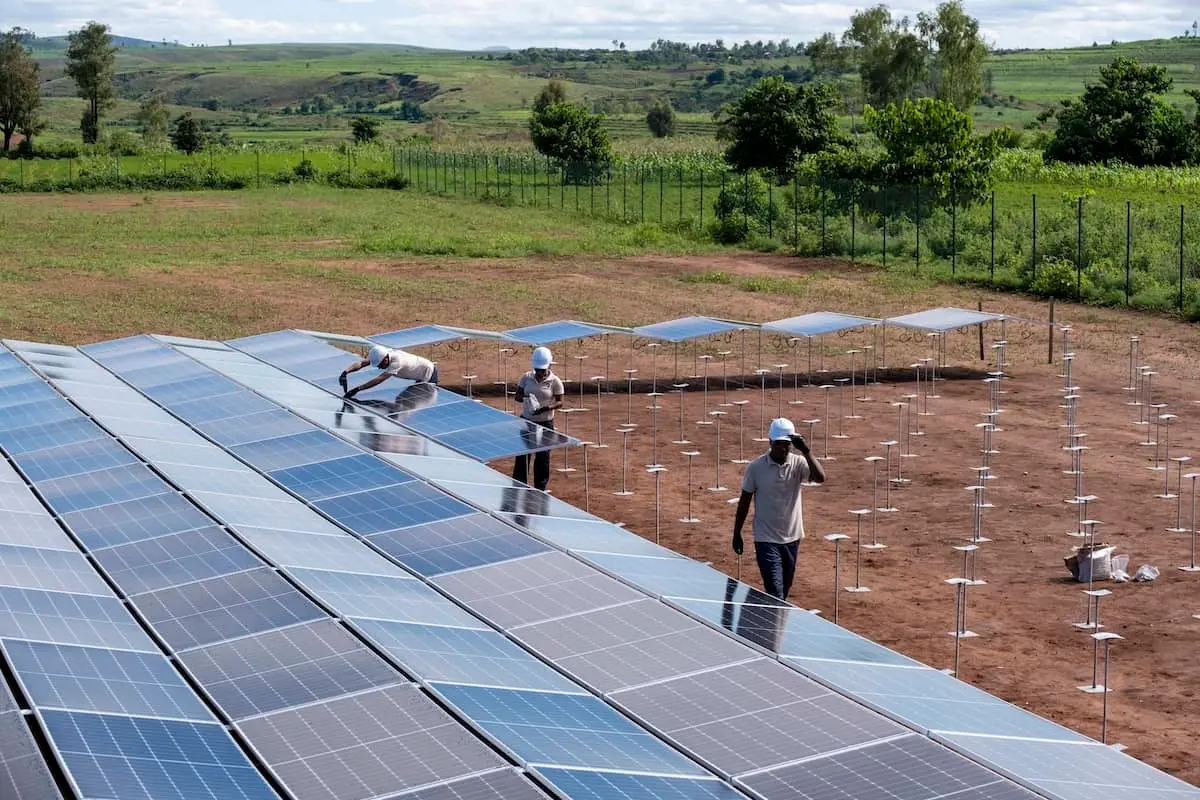 Arbeiter installieren Solarmodule auf einer großen Freiflächenanlage in einem ländlichen Feld.