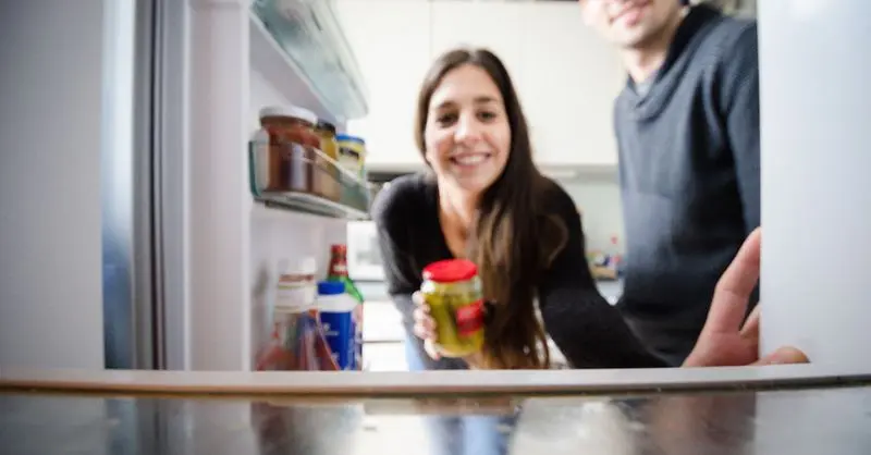Frau hält Gurkenglas in der Hand und schaut in den Kühlschrank