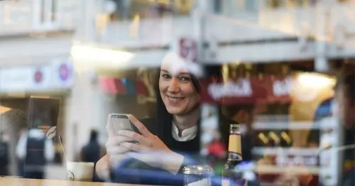 Smiling woman with smartphone, seen through a reflective cafe window.