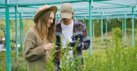 Eine Frau und ein Mann stehen in einem Gemeinschaftsgarten voller Pflanzen.