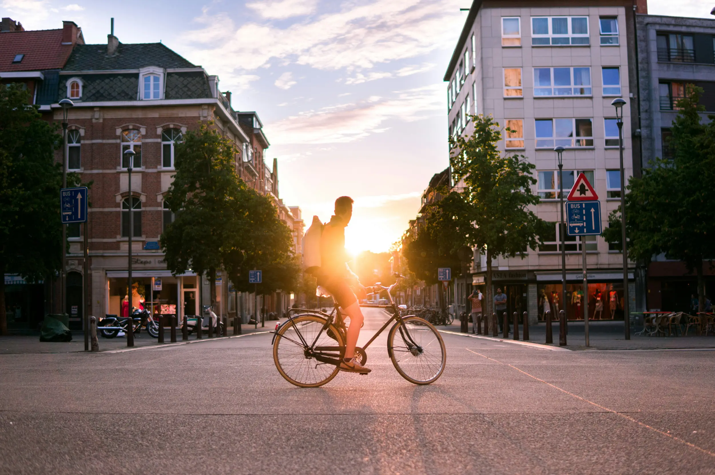 Ein Mann sitzt auf einem Fahrrad an einer leeren Kreuzung im Sonnenuntergang.