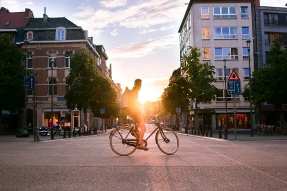 Ein Mann sitzt auf einem Fahrrad an einer leeren Kreuzung im Sonnenuntergang.