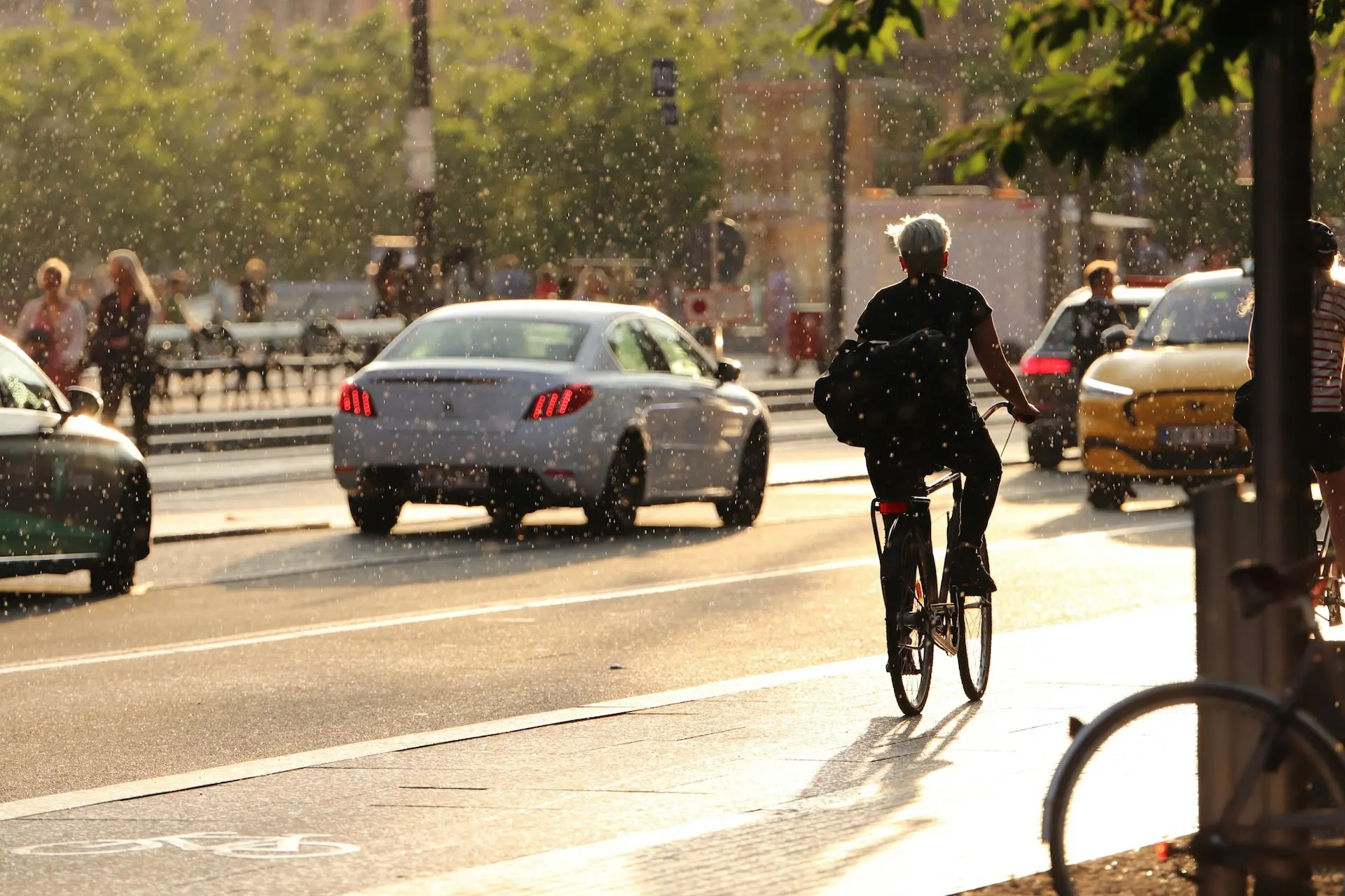Gegenlichtszene mit einem Radfahrer und Autos auf einer Stadtstraße, mit leuchtenden Partikeln, die in der Luft sichtbar sind.