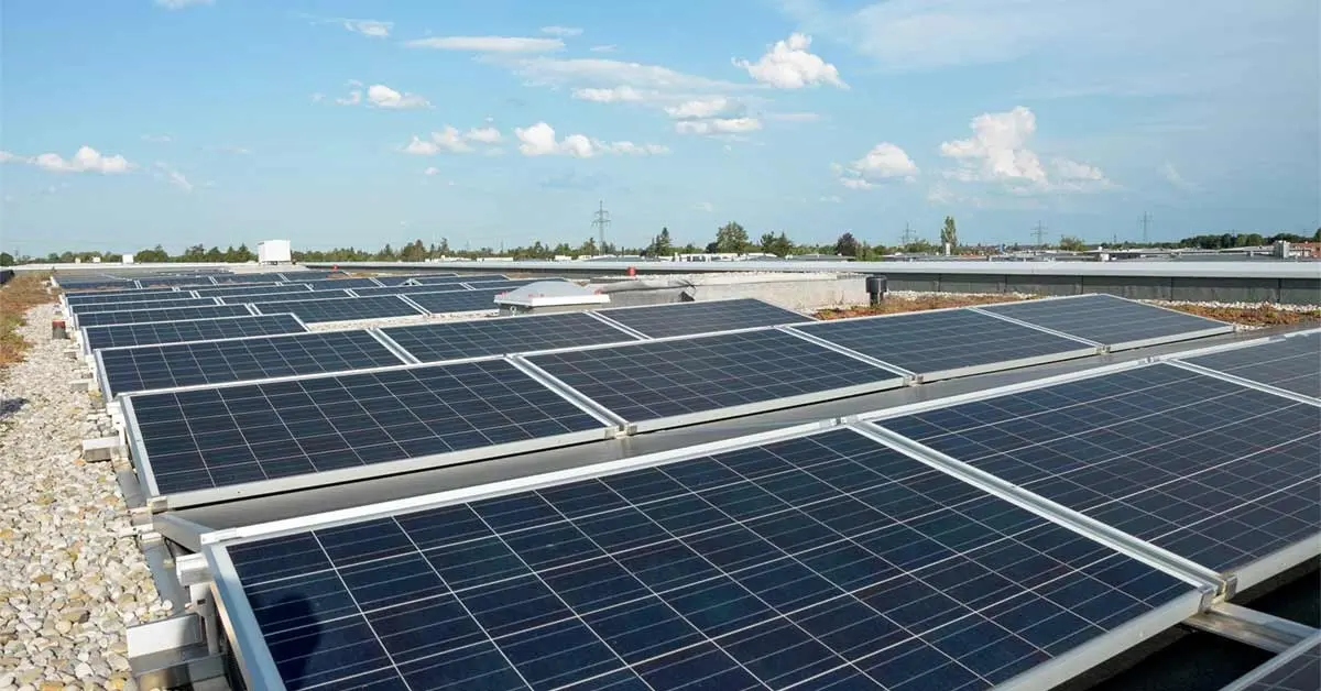 Solar panels installed on a gravel rooftop under a blue sky.